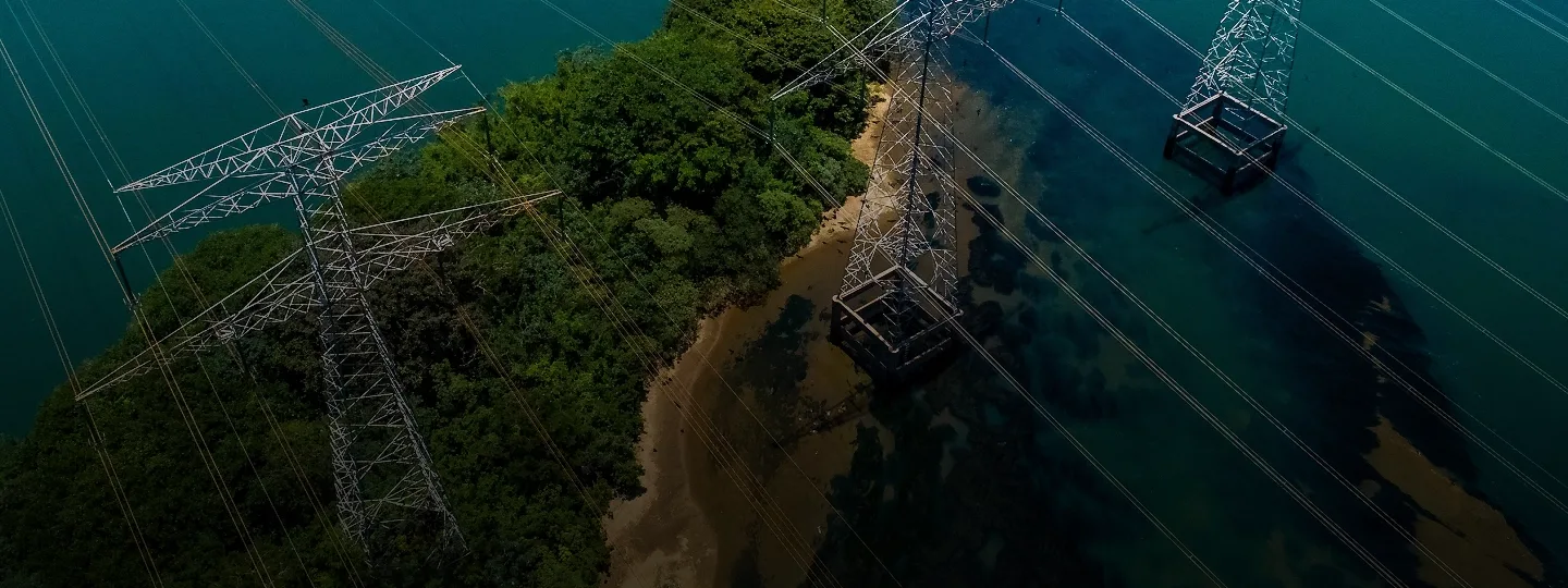 Luftaufnahme von Strommasten und Übertragungsleitungen in der Nähe von Wasser und Vegetation