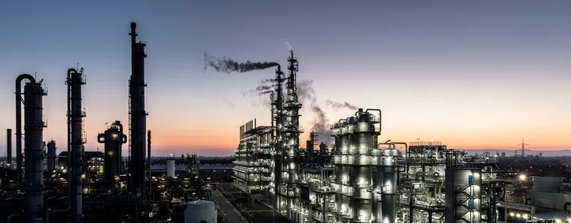 Beleuchtete Türme und Rohrleitungen einer Chemieanlage in der Abenddämmerung